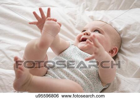 Stock Photograph - Baby girl (12-17 months) lying down with arms and legs up. Fotosearch