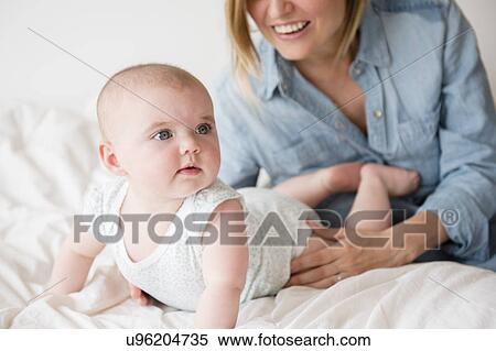 Stock Photography - Baby girl (12-17 months) with mother on bed. Fotosearch