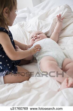 Baby girl (12-17 months) with sister (2-3) on bed View Large Photo Image Stock Photo - Baby girl (12-17 months) with sister (2-3) on bed. Fotosearch