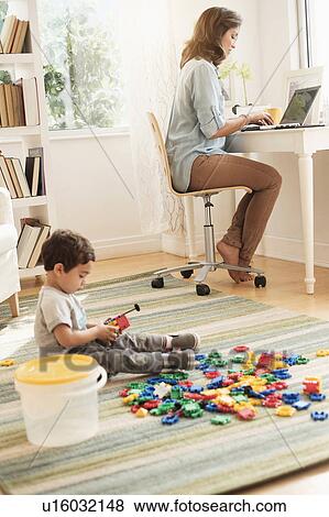 Boy (2-3) playing with toy blocks while mother working on laptop View Large Photo Image Stock Photo - Boy (2-3) playing with toy blocks while mother working on laptop. Fotosearch
