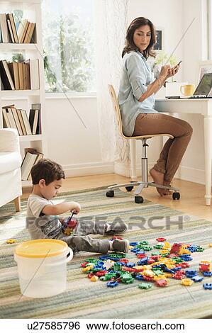 Boy (2-3) playing with toy blocks while mother working on laptop View Large Photo Image Stock Photograph - Boy (2-3) playing with toy blocks while mother working on laptop. Fotosearch