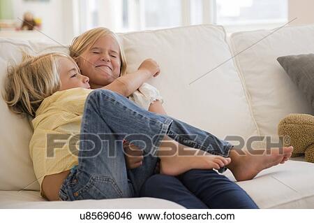 Stock Photograph - Boy (4-5) and girl (6-7) hugging on sofa. Fotosearch