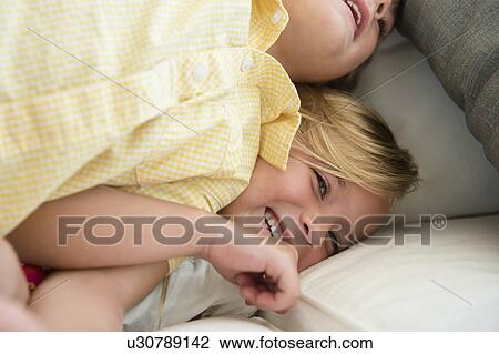 Stock Image - Boy (4-5) and girl (6-7) playing on sofa. Fotosearch