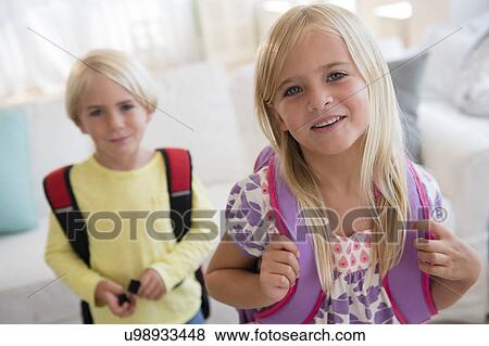 Stock Photo - Boy (4-5) and girl (6-7) with backpacks, looking at camera. Fotosearch