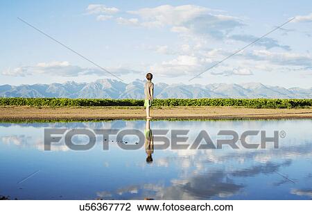 Stock Image - Boy (6-7) standing at water's edge. Fotosearch
