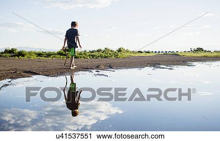 Stock Image - Boy (6-7) walking on lake shore. Fotosearch