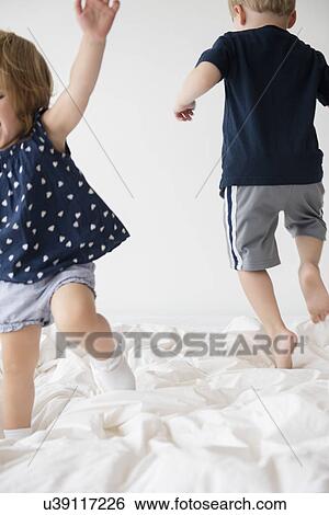 Stock Photograph - Brother (2-3) with sister (2-3) jumping on bed. Fotosearch
