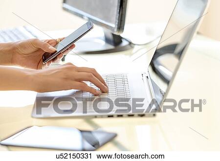 Stock Image - Business woman texting and typing on laptop keyboard. Fotosearch
