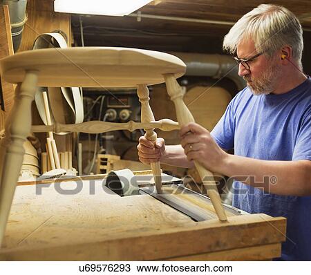 Stock Image - Carpenter polishing chair with sander. Fotosearch
