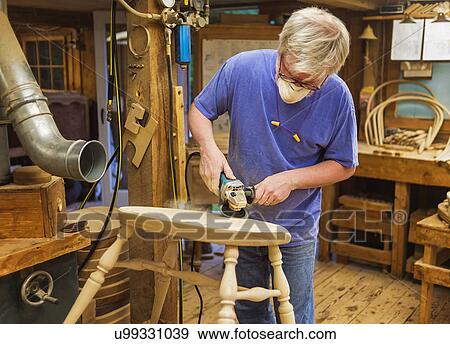 Stock Photo - Carpenter polishing chair with sander. Fotosearch