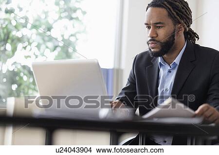 Concentrated businessman working with laptop at desk in office View Large Photo Image Picture - Concentrated businessman working with laptop at desk in office. Fotosearch