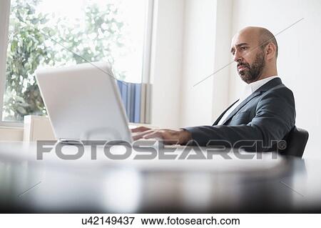 Concentrated businessman working with laptop at desk in office View Large Photo Image Stock Photo - Concentrated businessman working with laptop at desk in office. Fotosearch