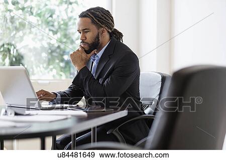 Stock Photo - Concentrated businessman working with laptop at desk in office. Fotosearch