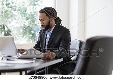 Concentrated businessman working with laptop at desk in office View Large Photo Image Stock Photograph - Concentrated businessman working with laptop at desk in office. Fotosearch