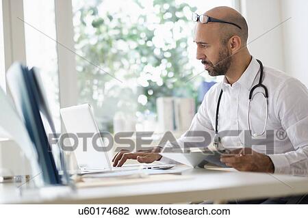 Concentrated doctor working with laptop at desk in office View Large Photo Image Stock Image - Concentrated doctor working with laptop at desk in office. Fotosearch