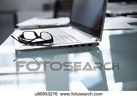 Stock Photograph - Eyeglasses and laptop on desk in office. Fotosearch
