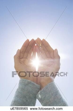 Stock Photography - Female hands against clear sky, sun shining through fingers. Fotosearch