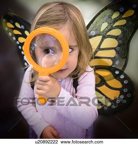 Stock Image - Girl (2-3) wearing butterfly wings looking through magnifying glass. Fotosearch