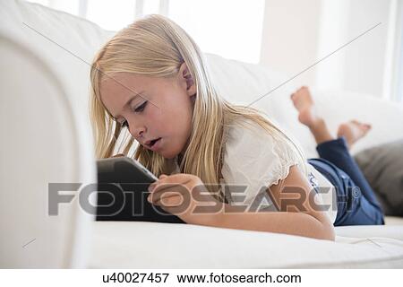 Stock Photo - Girl (6-7) using digital tablet on sofa. Fotosearch