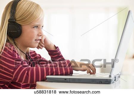 Stock Photo - Girl (6-7) wearing earphones, using laptop. Fotosearch