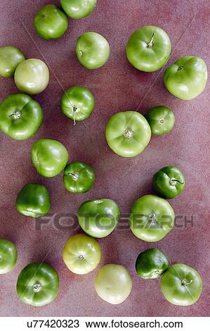 Stock Image - Green tomatillos on red background. Fotosearch