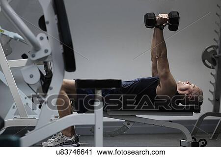 Stock Image - Man exercising with dumbbells on weight bench. Fotosearch