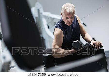 Stock Photo - Man exercising with dumbbells on weight bench. Fotosearch