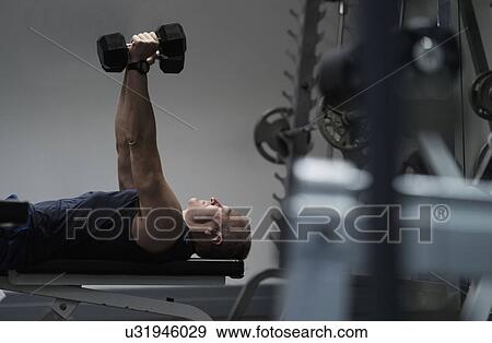 Stock Photo - Man exercising with dumbbells on weight bench. Fotosearch