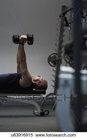 Stock Photography - Man exercising with dumbbells on weight bench. Fotosearch