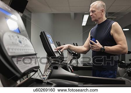 Stock Image - Man in health club adjusting treadmill before training. Fotosearch