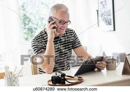 Man in home office using smartphone and tablet View Large Photo Image Stock Photo - Man in home office using smartphone and tablet. Fotosearch