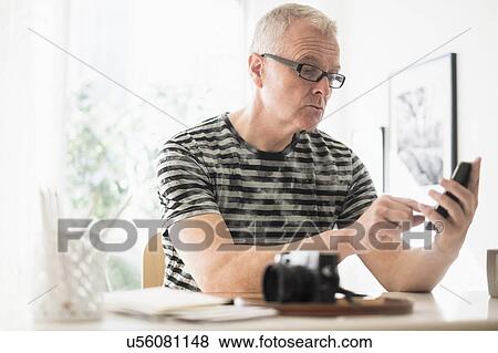 Stock Photo - Man in home office using smartphone. Fotosearch