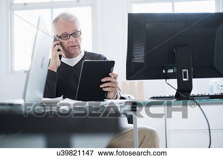 Stock Photo - Man in office using smartphone and tablet. Fotosearch