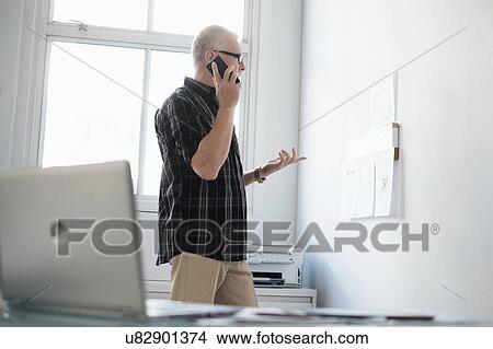 Picture - Man in office using smartphone. Fotosearch