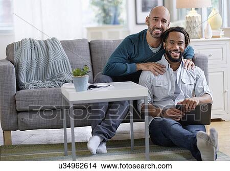 Picture - Man massaging boyfriend by sofa in living room. Fotosearch