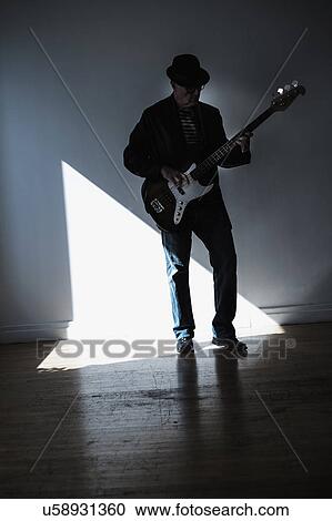Stock Image - Man playing bass guitar in empty room. Fotosearch