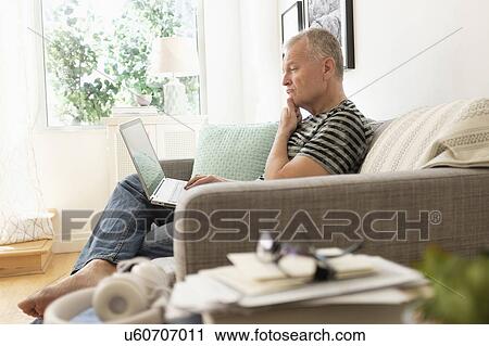 Stock Image - Man sitting on sofa using laptop. Fotosearch
