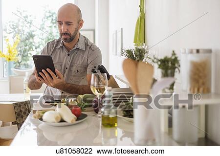 Man using digital tablet leaning on kitchen counter View Large Photo Image Stock Image - Man using digital tablet leaning on kitchen counter. Fotosearch