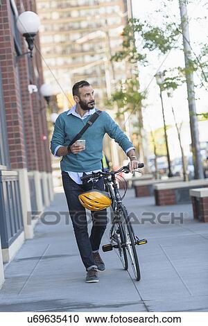 Stock Image - Man walking with bicycle in city. Fotosearch
