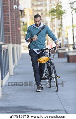 Stock Photography - Man walking with bicycle using phone. Fotosearch