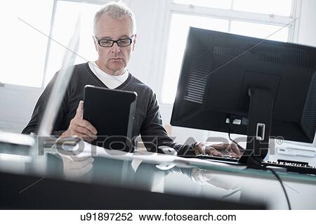 Man working in office using computer and tablet View Large Photo Image Stock Image - Man working in office using computer and tablet. Fotosearch