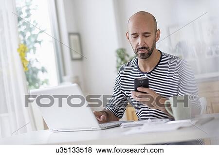 Man working with laptop and holding smart phone at table View Large Photo Image Stock Photo - Man working with laptop and holding smart phone at table. Fotosearch
