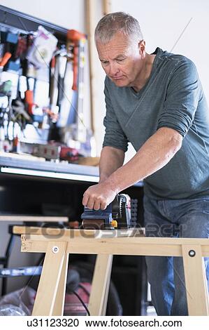 Stock Image - Man working with wood in home workshop. Fotosearch