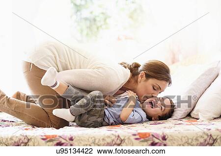 Stock Image - Mother playing with son (2-3) on bed. Fotosearch