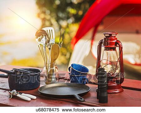 Stock Photography - Oil lamp, binoculars and cooking utensils on picnic table. Fotosearch