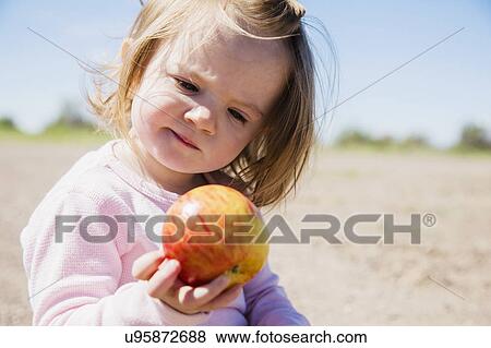 Stock Photo - Portrait of girl (2-3) holding apple. Fotosearch