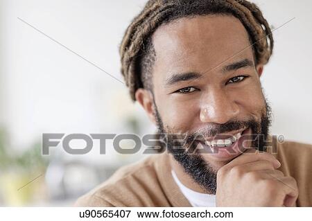 Stock Photo - Portrait of smiley young man with hand on chin. Fotosearch