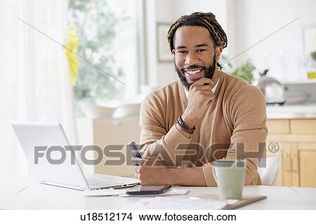 Portrait of smiley young man with laptop at table View Large Photo Image Picture - Portrait of smiley young man with laptop at table. Fotosearch