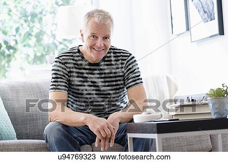 Stock Image - Portrait of smiling man sitting on sofa at home. Fotosearch