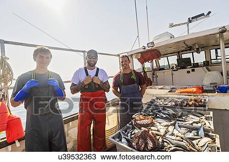 Stock Image - Portrait of three fishermen standing on boat. Fotosearch
